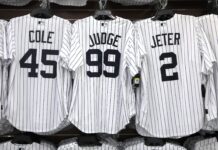 Yankees Make Bold Decision To Break 108-Year Tradition Row of white pinstripe baseball jerseys on a rack, showing names COLE (45) on the left and JETER (2) on the right, with a center jersey displaying number 99.