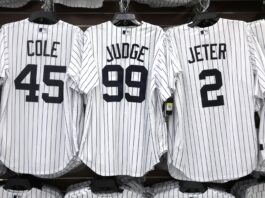 Row of white pinstripe baseball jerseys on a rack, showing names COLE (45) on the left and JETER (2) on the right, with a center jersey displaying number 99.