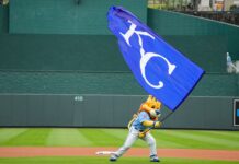 MLB Team Announces Plans for $1.9 BILLION Downtown Stadium Mascot in blue uniform runs with a large blue flag bearing white lettering on a baseball field.