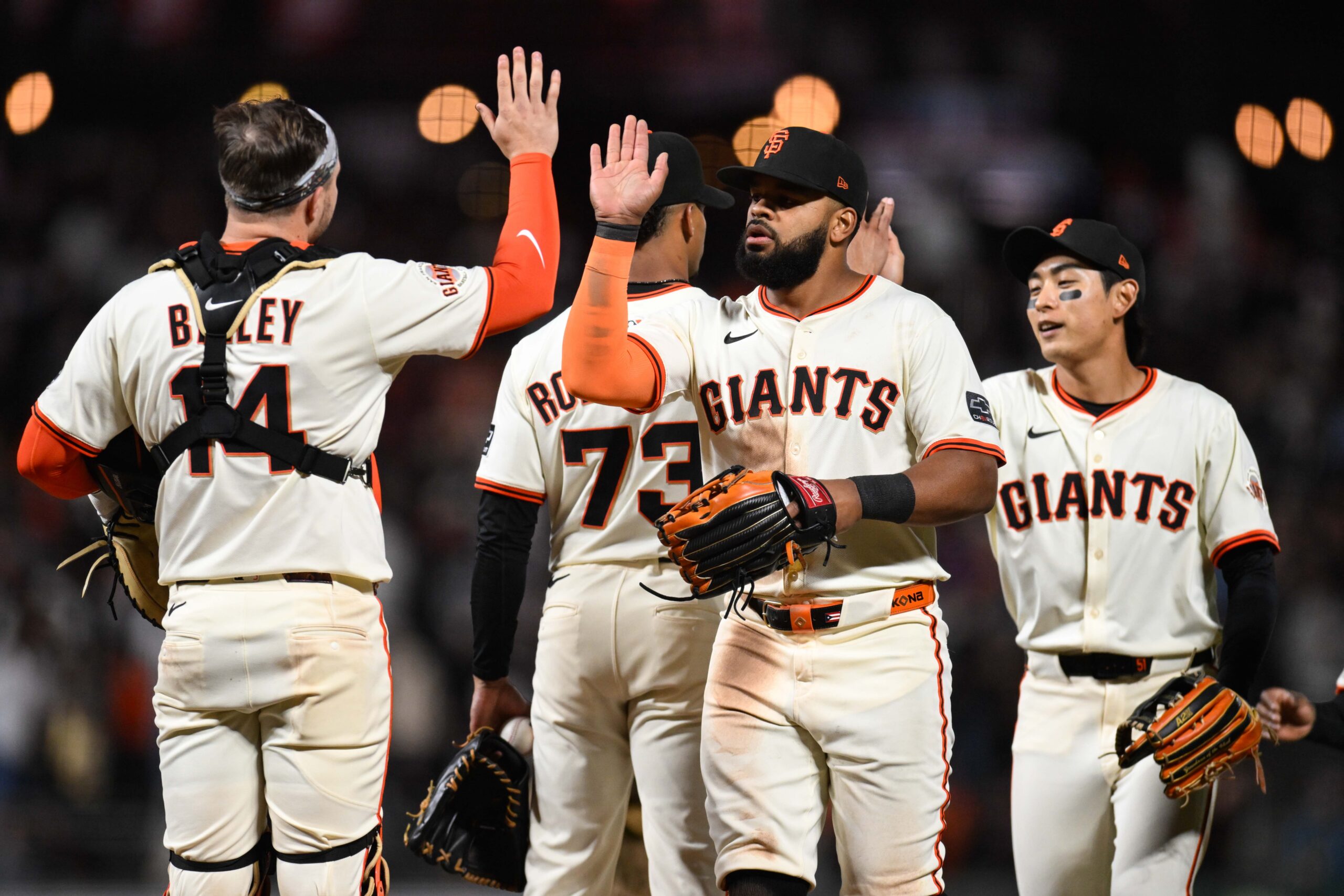 MLB Team Stuns Fans With Wild Sexual Celebration San Francisco Giants players in white uniforms high-five each other on the field after a play, with one wearing a glove and others smiling.