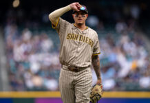 MLB All-Star Gets Into It With Reporter Baseball player in a tan pinstripe San Diego Padres uniform saluting with his right hand on a blurred crowd background, during a game.