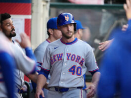 New York Mets Ditch ex-Yankees Flop After Just a Month Baseball player in a gray New York Mets uniform wearing a blue helmet with an orange NY logo, standing in the dugout with teammates nearby.