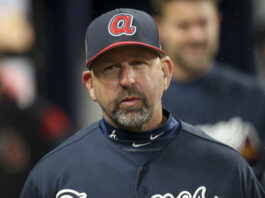 Baseball coach wearing a navy uniform and cap with a red A logo, looking serious in a rainy scene.