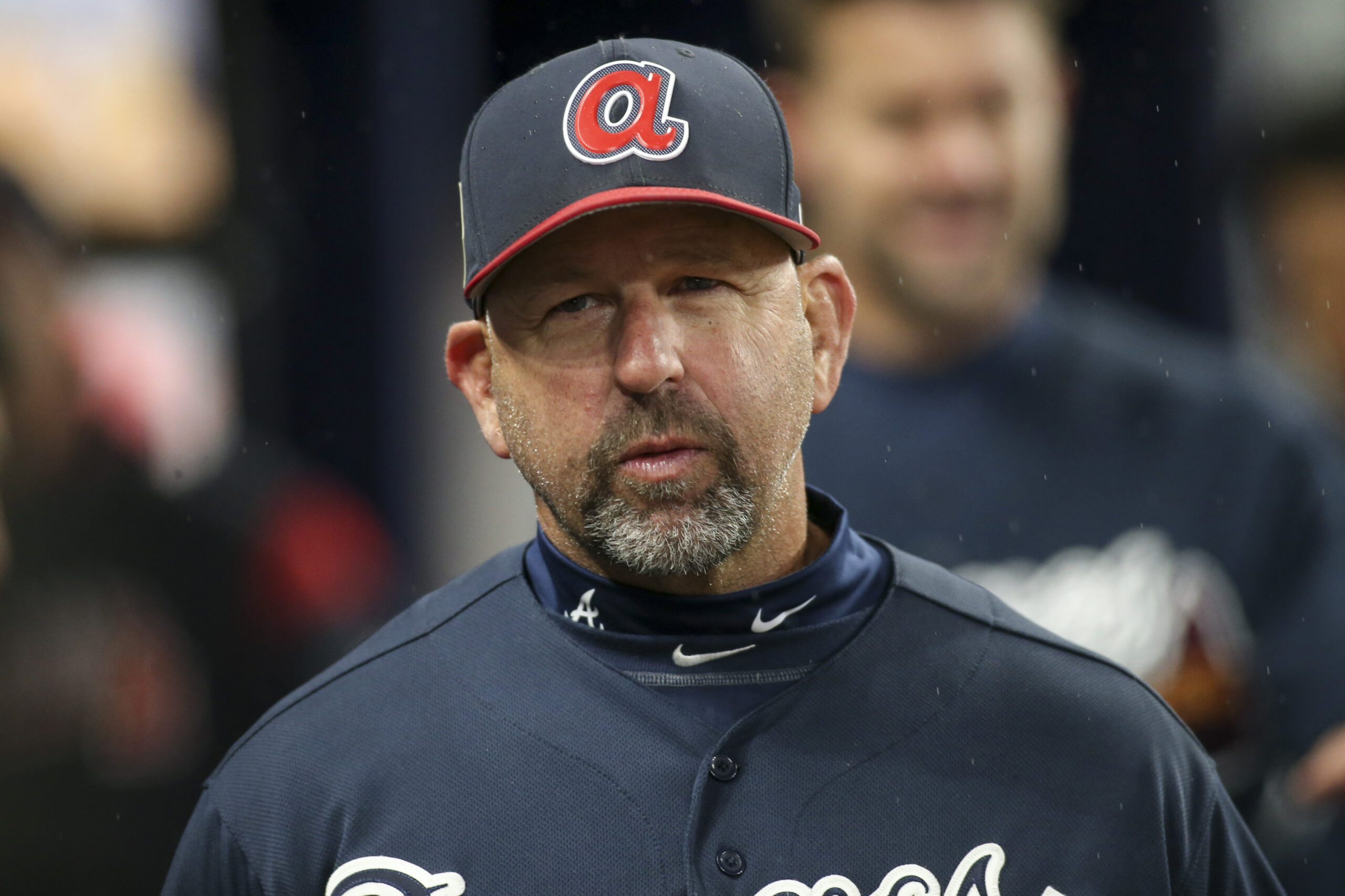 Baseball coach wearing a navy uniform and cap with a red A logo, looking serious in a rainy scene.
