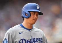 Shohei Ohtani Exits Dodgers Game With Scary Injury Baseball player wearing a blue Dodgers helmet and gray uniform, looking to the right with a blurred stadium background.