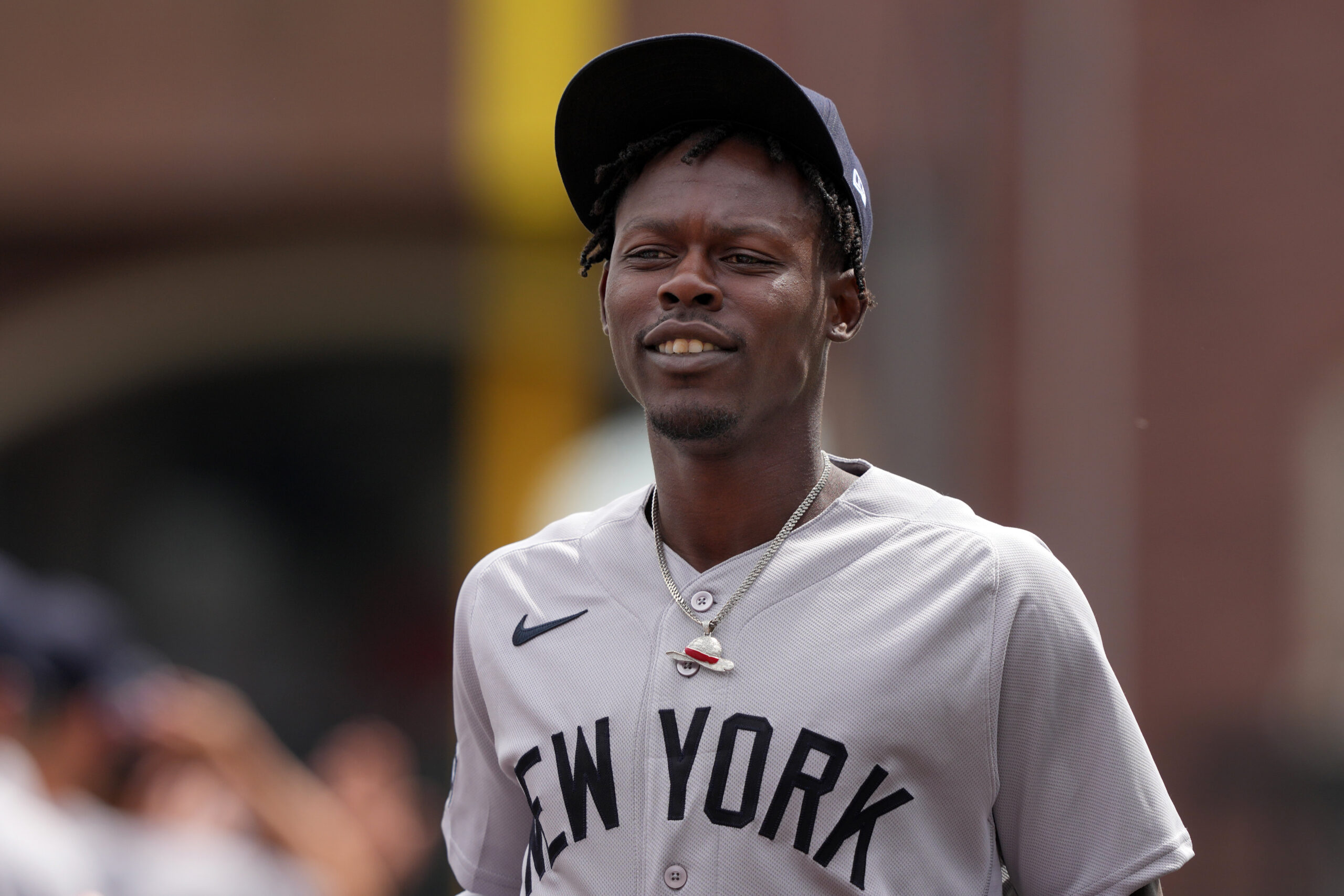 Baseball player in a gray New York jersey and black cap, smiling slightly outdoors.