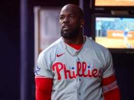Portrait of a Black man wearing a Philadelphia Phillies baseball jersey with a silver chain, indoors.