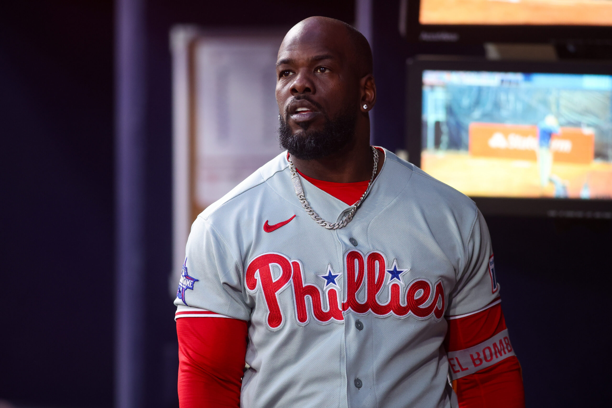 Portrait of a Black man wearing a Philadelphia Phillies baseball jersey with a silver chain, indoors.