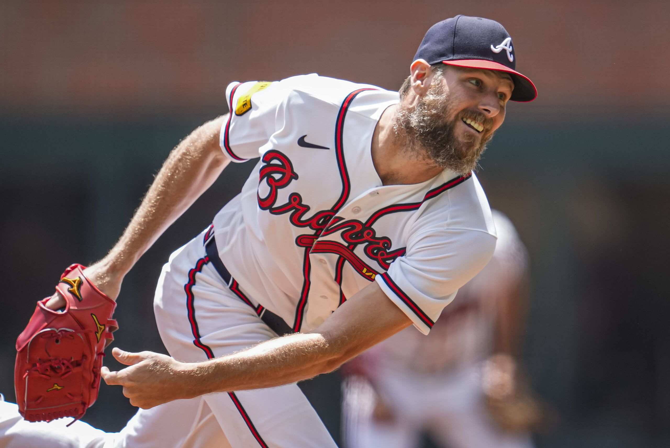 Baseball pitcher in Braves uniform mid-throw with a red glove extended