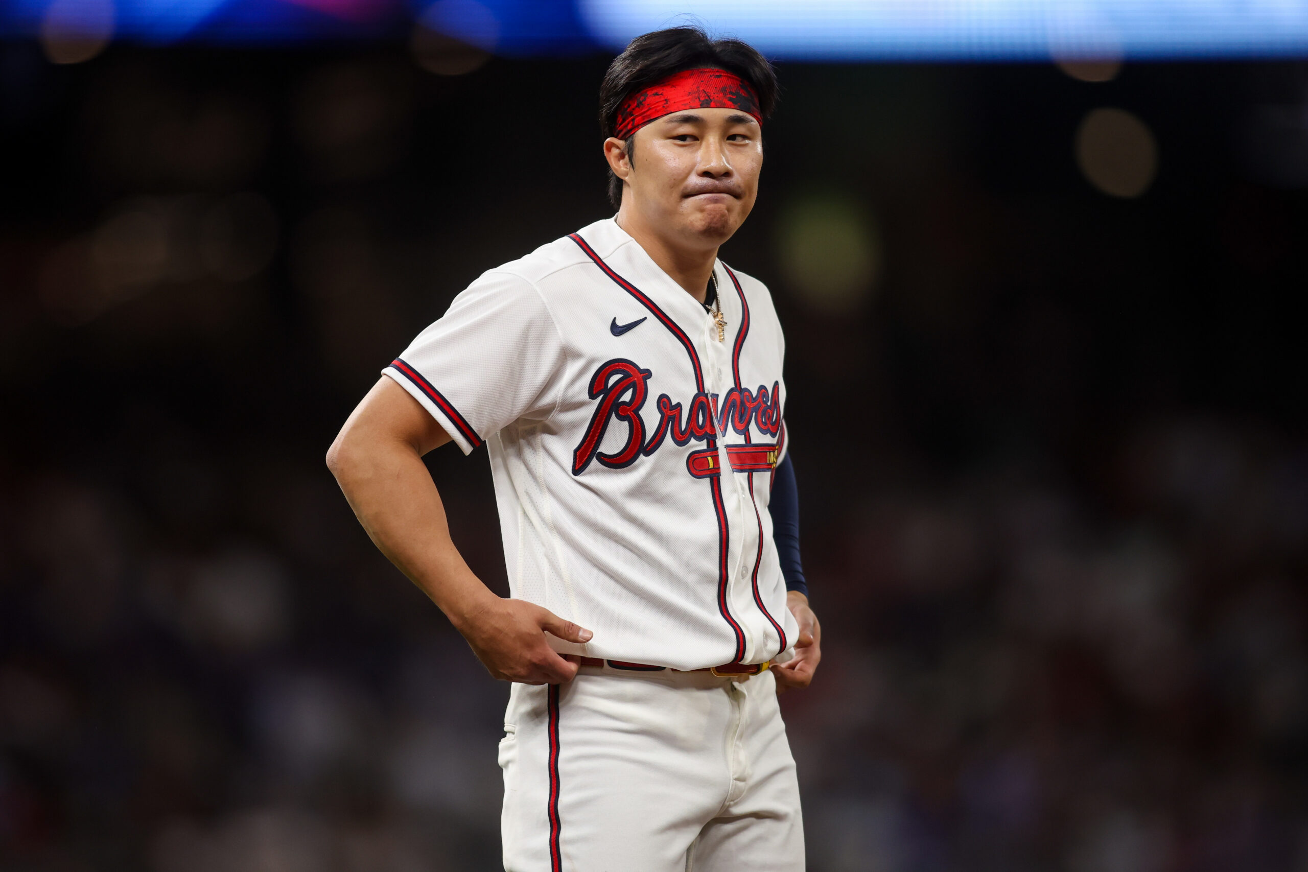 Baseball player in a Braves uniform with a red headband standing with hands on hips on the field, focused expression