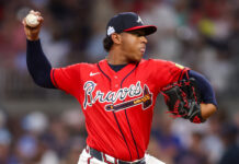 The Youngest Pitcher In MLB May Be The Braves’ Next Star Braves pitcher mid-throw in a red jersey and navy cap, ball raised ready to throw