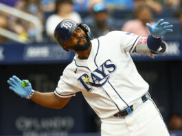 Rays Star Makes MLB History After Latest Home Run Baseball player in a white uniform with blue accents and blue gloves reaches forward during a play, wearing a dark helmet.