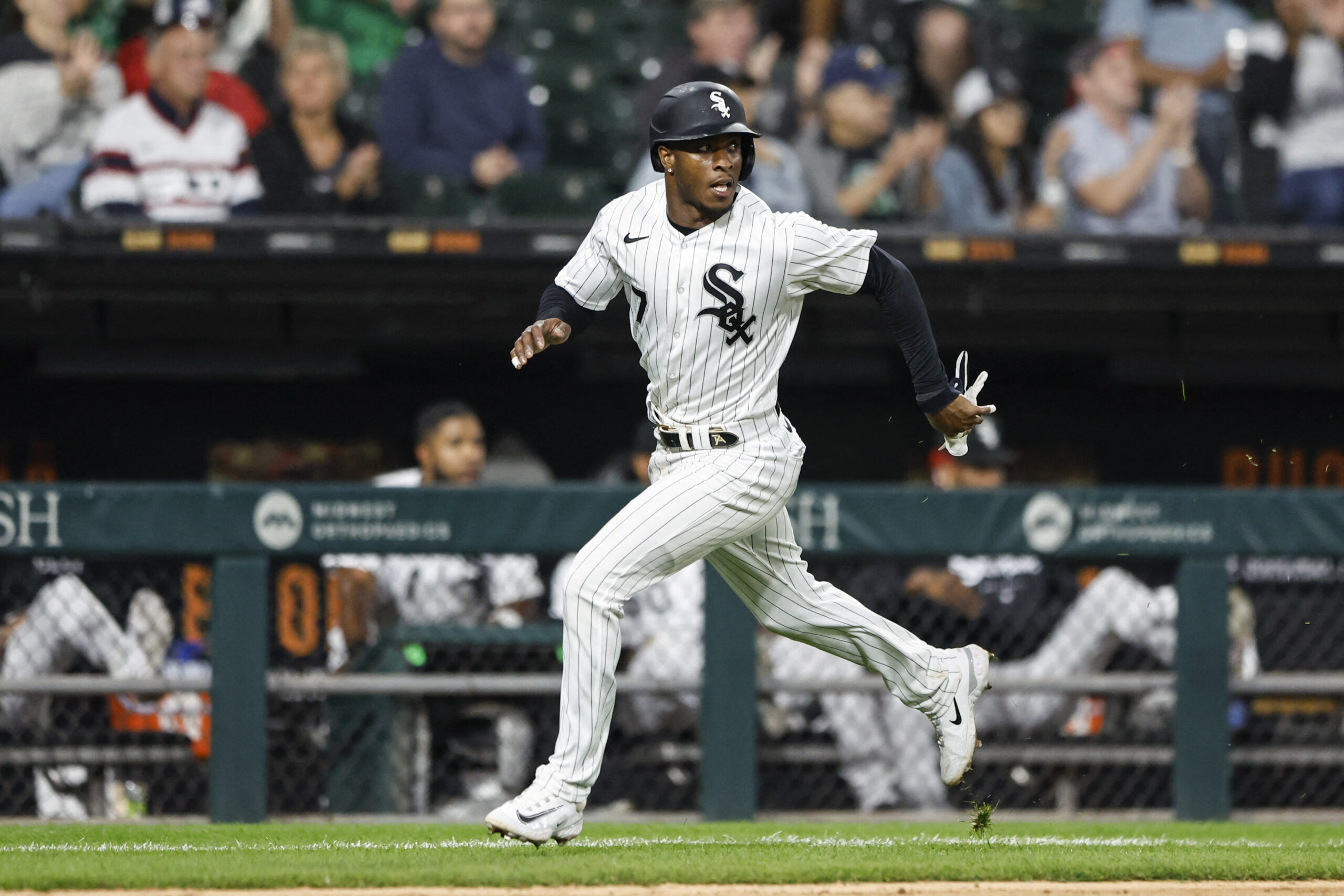 Baseball player in a white pinstripe White Sox uniform running on the field with a ballpark crowd in the background, mid-stride in a game.