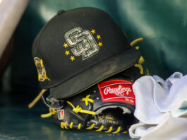 Black baseball glove with bright yellow laces and a Rawlings patch resting on a teal surface, cap perched nearby.
