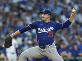 Dodgers pitcher in blue uniform throwing a pitch during a game with a blurred stadium crowd in the background