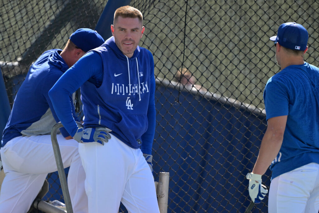 Baseball players in blue uniforms stand near a chain-link fence during practice.