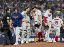 Group of Boston Red Sox players and an umpire standing on a pitcher's mound during a game, with a crowded stands in the background